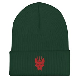 Puede incluir: Un gorro de lana verde oscuro con un logotipo rojo bordado de una calavera con un tridente en la parte superior.
