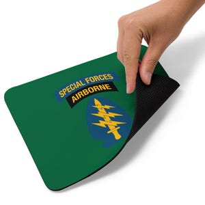 May include: Green rectangular mousepad with the words "SPECIAL FORCES AIRBORNE" in yellow and white text. The mousepad features a blue and yellow emblem. The bottom of the mousepad is black.