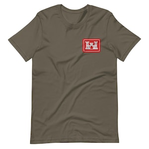 May include: Olive green t-shirt with a small embroidered patch on the upper left chest. The patch features a white castle design within a red rectangular border. The shirt has short sleeves and a crew neck.
