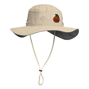 May include: A beige sun hat with a wide brim and a dark gray underside. The hat features a mesh panel and a chin strap. An embroidered jack-o'-lantern design is on the front. The hat is designed for sun protection.
