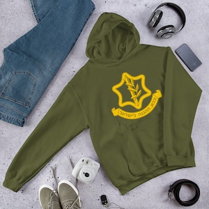 Può includere: Una felpa con cappuccio verde con un emblema ricamato giallo del logo delle Forze di Difesa Israeliane (IDF). Il logo presenta una stella a sei punte con una spada e un ramo di ulivo all'interno. Il testo sul nastro recita "צה"ל  הגנה לישראל" che si traduce in "IDF - Difesa di Israele".