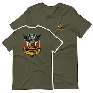 May include: Olive green t-shirts with a graphic featuring a coiled yellow snake, crossed rifles, and the text "Don't Tread on Me." The design is on the front and a smaller version on the upper chest. The shirts are made of a soft material.