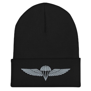 Peut inclure: Bonnet noir avec un motif brodé gris d'un parachute et d'ailes. Le bonnet est fait d'un matériau tricoté doux. Le motif est centré sur le devant du chapeau. Un accessoire idéal pour l'hiver.