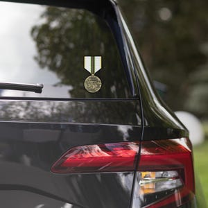 May include: A black car with a sticker of a military medal on the back window. The medal is gold with a green, white, and black ribbon.