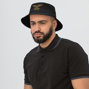May include: Black bucket hat featuring a gold embroidered eagle and the word "Rangers". The hat has a wide brim. The person is wearing a black polo shirt.