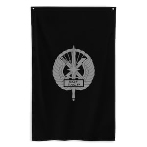 以下が含まれることがあります： 黒い旗に灰色のエンブレム。エンブレムには星、翼、稲妻が含まれ、「SOF TACP」の文字があります。旗は長方形で垂直に吊り下げられ、上部に吊り下げ用のグロメットが付いています。デザインは旗の中央に配置されています。