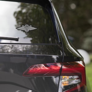 Może przedstawiać: Czarny samochód z srebrną naklejką przedstawiającą skrzydlaty emblemat na tylnej szybie. Emblemat zawiera miecz i gwiazdę w środku.
