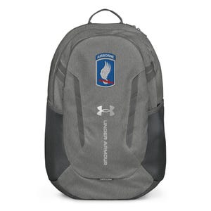 May include: Grey Under Armour backpack featuring the word "AIRBORNE" above a patch with a blue and white design. The Under Armour logo is below the patch, and the words "UNDER ARMOUR" are printed vertically. The backpack has side mesh pockets.