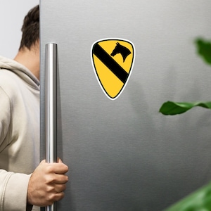 Könnte beinhalten: Ein gelber, schwarzer und grüner schildförmiger Aufkleber mit einer schwarzen Pferdekopf-Silhouette. Der Aufkleber hat einen schwarzen diagonalen Streifen und einen grünen Rand. Der Aufkleber wird auf einer silbernen Kühlschranktür angezeigt.