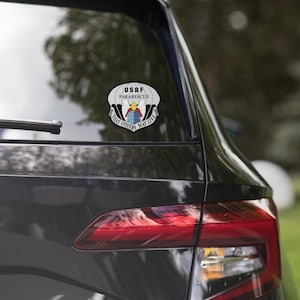 May include: A sticker featuring the USAF Pararescue emblem, with a parachute design and the text "THAT OTHERS MAY LIVE." The emblem includes a globe, wings, and the words "USAF Pararescue."