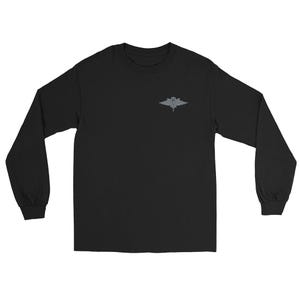 May include: Black long-sleeve shirt with a small, gray emblem on the upper left chest. The emblem appears to be a stylized design, possibly a crest or logo. The shirt has a crew neck and long sleeves.