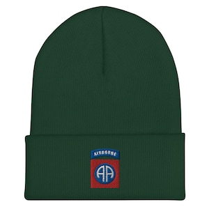 May include: A dark green beanie with a red, white, and blue embroidered patch that says "AIRBORNE" and has a white "AA" inside a blue circle.
