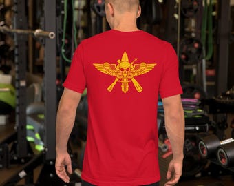 May include: A red short-sleeved t-shirt featuring a yellow graphic on the back. The design displays a central skull with wings, a vertical dagger, and two crossed rifles, creating a symmetrical emblem centered on the upper back area.