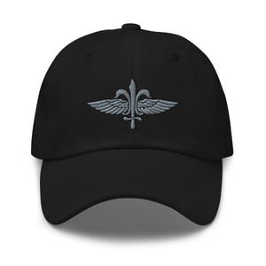 May include: A black baseball cap featuring an embroidered gray emblem on the front. The design consists of a central vertical sword flanked by two symmetrical wings, with a fleur-de-lis motif integrated into the upper portion of the sword.