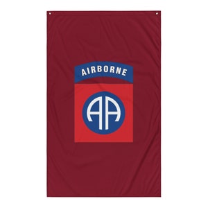 May include: A maroon flag with a blue and red patch. The patch has the words "AIRBORNE" in white lettering and a blue circle with the letters "AA" in white inside.