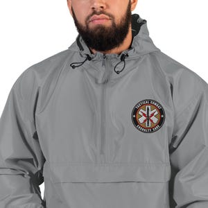 May include: A gray windbreaker jacket with a hood and a half-zip closure. The jacket features an embroidered patch on the left chest with the words "TACTICAL COMBAT" and "CASUALTY CARE" surrounding a medical symbol.