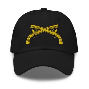Puede incluir: Gorra de béisbol negra con un diseño bordado en oro de dos pistolas cruzadas. La gorra tiene una visera curva y una correa ajustable. Las pistolas están detalladas con diseños intrincados.