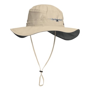 May include: A beige sun hat with a gray underside and a black adjustable chin strap. The hat features a graphic of a military aircraft on the front.