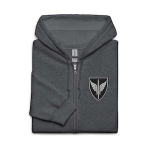 May include: A dark heather gray zip-up hoodie featuring a hood with drawstrings and a full-length front zipper. On the left chest, there is a black shield-shaped patch with an embroidered white design of a sword centered between two wings.