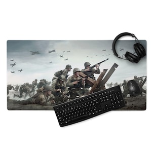 Puede incluir: Alfombrilla de ratón rectangular con una escena de guerra con soldados, aviones y alambre de púas. Un teclado, un ratón y unos auriculares negros están sobre una superficie blanca.