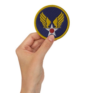 Può includere: Una toppa ricamata blu e gialla con una stella rossa e bianca e ali. La toppa è tenuta in una mano.