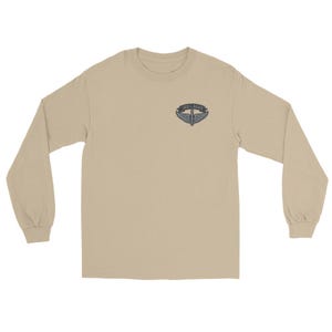 May include: A long-sleeved, tan-colored shirt. The shirt features a small emblem on the upper left chest area. The emblem has the words "180th SOAR" and a design of wings and a shield.