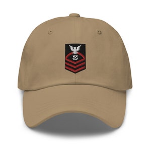 May include: A tan baseball cap with an embroidered patch featuring a white eagle, a black anchor, and red stripes. The patch is a US Navy rank insignia.