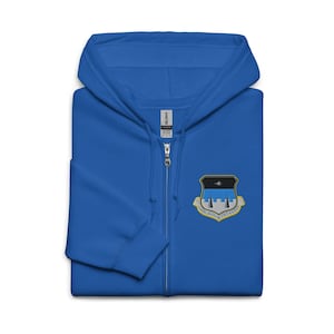 May include: A royal blue zip-up hoodie with a hood and a small embroidered emblem on the chest. The emblem features a black and gold shield with a star and three towers. The hoodie has a full zipper and a tag that says "Gildan".