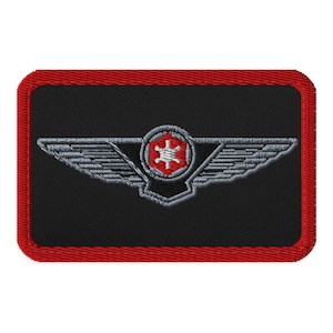 May include: Embroidered patch with a black background and a red border. The patch features a silver-colored wing design with a central emblem in a red hexagon shape, containing a white starburst.