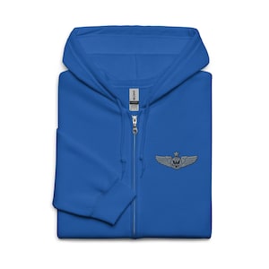 May include: A royal blue zip-up hoodie with a hood and a small embroidered emblem on the chest. The emblem features a skull with wings and a star above it. The hoodie has a full-length zipper and a soft texture.