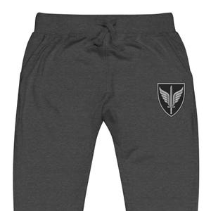 May include: Dark charcoal gray sweatpants featuring an elastic waistband with a matching drawstring. On the right thigh, there is an embroidered patch displaying a black shield containing a silver sword with wings extending from the sides.