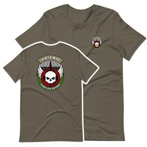 Może przedstawiać: Zielone koszulki w kolorze oliwkowym z graficznym wzorem przedstawiającym czaszkę, skrzydła oraz napisy "AIR TO MUD" i "CLOSE AIR SUPPORT". Projekt jest w kolorze białym, czerwonym i zielonym. Koszulki są z krótkim rękawem.