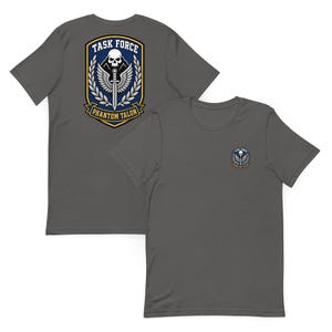 Può includere: Due magliette grigie con l'emblema "Task Force Phantom Talon". L'emblema presenta un teschio, una spada e ali, con testo in un design a scudo. Una maglietta mostra l'emblema sul davanti, l'altra sul retro.