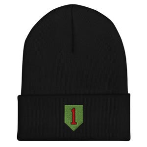 May include: A black knit beanie featuring a folded cuff. Centered on the cuff is an embroidered patch in the shape of a shield with a light green background and a bold red number one stitched in the center of the shield emblem.