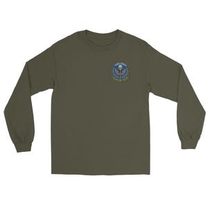 May include: Olive green long-sleeve shirt with a crew neck. The shirt features a circular emblem on the upper left chest with the words "TASK FORCE" above a skull and wings design, and "PHANTOM TALON" below. The emblem is in shades of blue, white, and gold.