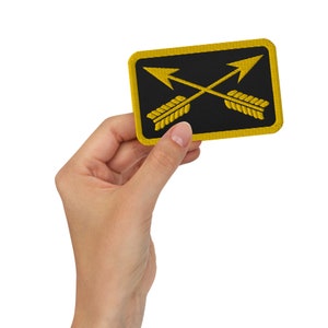 May include: A yellow embroidered patch with two crossed arrows on a black background. The patch is rectangular with a yellow border.