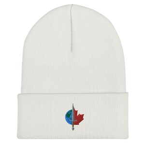 Könnte beinhalten: Weiße Strickmütze mit einem roten Ahornblatt und einem blauen Globus mit einem silbernen Schwert, das durch ihn hindurchgeht, auf der Vorderseite gestickt.