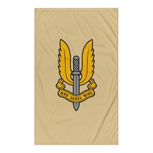 May include: Tan flag featuring a yellow and black emblem with a sword and wings design. The emblem includes the text "WHO DARES WINS" in a banner. The flag is rectangular and has a grommet at the top for hanging.