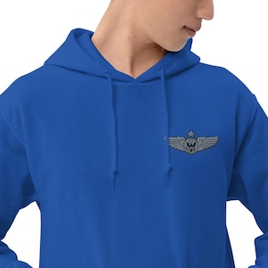 May include: Royal blue hoodie with a detailed embroidered emblem featuring a skull, wings, and a star. The hoodie has a drawstring hood and a kangaroo pocket. The emblem is located on the upper left chest.