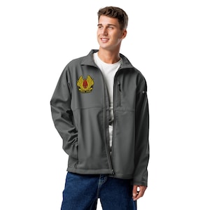 May include: A charcoal gray softshell jacket with a zip-up front, a small chest pocket, and a yellow and red emblem on the left chest. The jacket is worn over a white t-shirt and blue jeans.