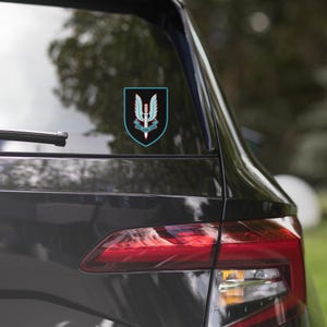 May include: A black car with a blue and white sticker of the Special Air Service (SAS) emblem on the back window. The emblem features a winged dagger with the words "Who Dares Wins" underneath.