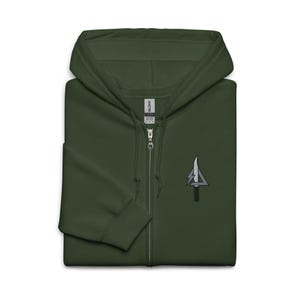 May include: A dark green zip-up hoodie with a small embroidered emblem on the left chest. The emblem features a knife, a lightning bolt, and a triangle. The hoodie has a full zipper and a hood.