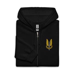May include: Black zip-up hoodie with a hood and a small embroidered emblem on the chest. The emblem features a yellow winged dagger design with the text "WHO DARES WINS" in yellow.