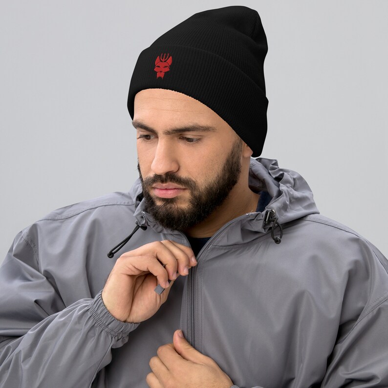 Puede incluir: Un gorro negro con un logotipo bordado en rojo de una cabeza estilizada con cuernos. El logotipo est&aacute; centrado en la parte delantera del gorro.