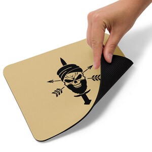 Könnte beinhalten: Ein braunes Mauspad mit einem schwarzen Schädel, der einen Turban und einen Dolch trägt. Der Schädel ist von vier Pfeilen umgeben. Das Mauspad hat eine schwarze Gummibeschichtung.