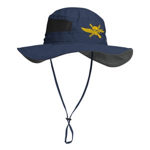 May include: A navy blue wide-brimmed sun hat featuring a black mesh ventilation panel on the side and a yellow embroidered emblem of a skull with wings and crossed rifles. The hat includes an adjustable chin strap with a sliding toggle fastener.