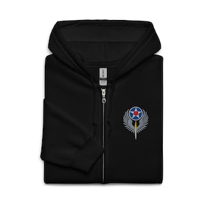 May include: Black zip-up hooded sweatshirt with an embroidered emblem on the left chest. The emblem features a blue star within a red circle, surrounded by silver wings and a yellow sword. The sweatshirt has a full zip and a hood.