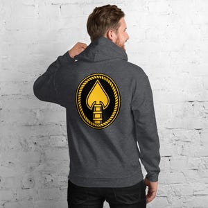 May include: Dark gray hooded sweatshirt with a large gold and black spade design on the back. The spade is inside a black circle, surrounded by a gold rope-like border. The hoodie has a drawstring and a front pocket.