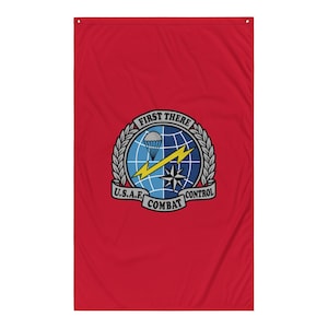 May include: A red flag featuring a circular emblem with the text "FIRST THERE" at the top. The emblem includes a globe, parachute, lightning bolt, and star, with "U.S.A.F. COMBAT CONTROL" at the bottom.