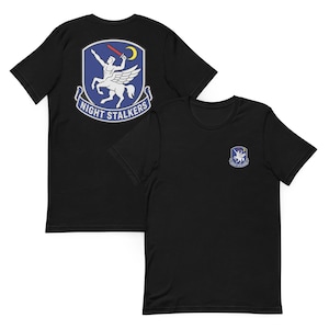 May include: A black short-sleeve t-shirt featuring a graphic on the front left chest and a larger version on the back. The graphic is a shield-shaped emblem with a white centaur, a red sword, a yellow crescent moon, and the text NIGHT STALKERS.